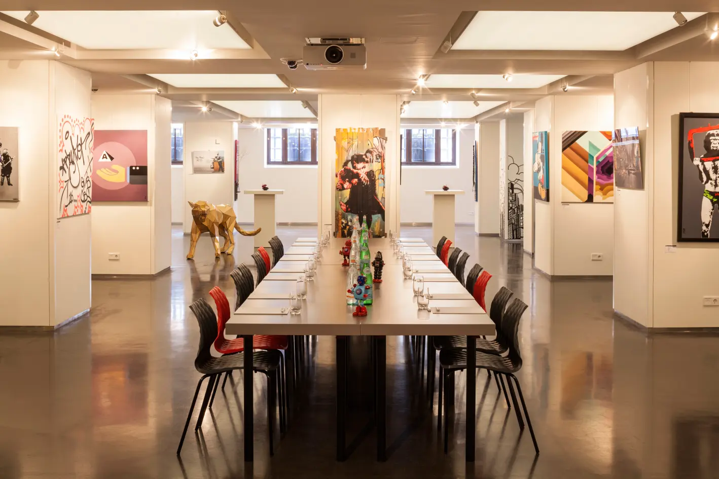 A modern art gallery featuring a long dining table with colorful decor, surrounded by various artworks on the walls.