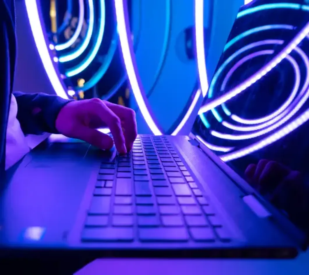 A hand typing on a laptop keyboard, illuminated by vibrant blue and purple circular lights in the background.