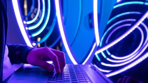 A hand typing on a laptop keyboard, illuminated by vibrant blue and purple circular lights in the background.