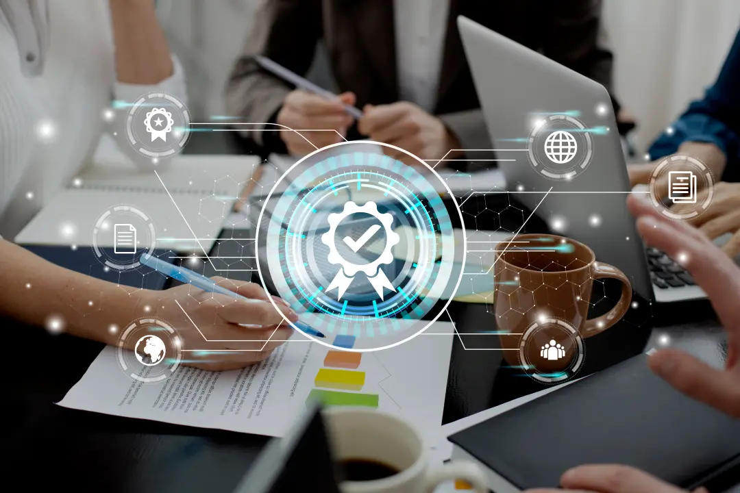 A group meeting with hands on documents and a laptop, featuring digital icons representing quality assurance and collaboration.